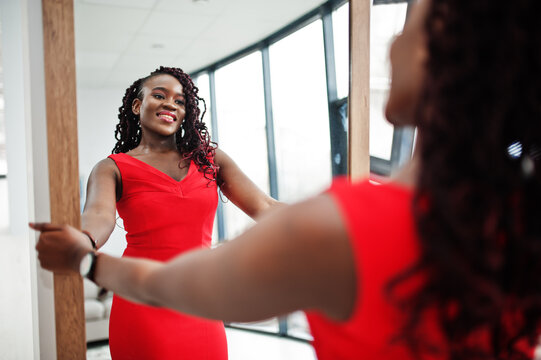 Magnificent young african woman in luxurious red dress in a luxury apartment look at mirror. Beauty, fashion.