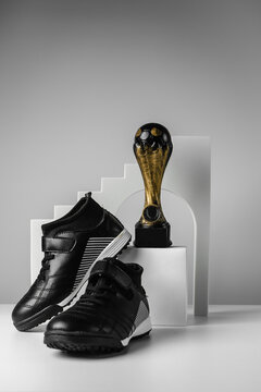 Sports shoes and a cup for the first place. Black sneakers on a gray background. Conceptual photo. Place for your text. 
Football prize. Cup on the podium. Trendy style