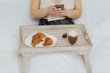 Cropped shot of woman with breakfast in bed in the morning, is using smartphone.