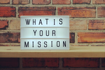 What is your mission word in light box on brick wall and wooden shelves background