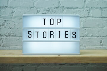 Top Stories word in light box on white brick wall and wooden shelves background