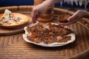 Close up of a hand putting spices on Manakish Lahm Bi Ajeen - Flatbreads with minced lamb or beef and Fatayer stuffed pie with spinach. Traditional Arab food