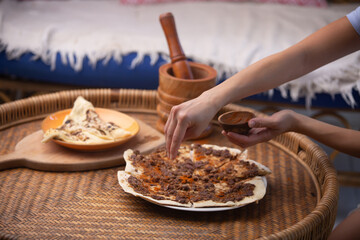 Close up of a hand putting spices on Manakish Lahm Bi Ajeen - Flatbreads with minced lamb or beef and Fatayer stuffed pie with spinach. Traditional Arab food
