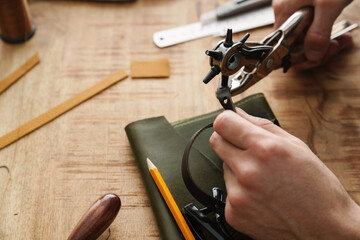 White craftsman using tool while working with leather in workshop