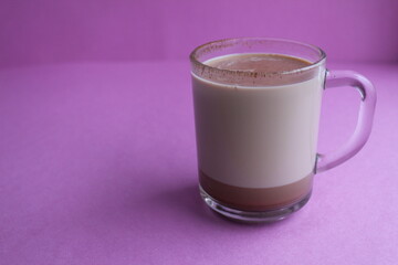a cup of hot chocolate cocoa in a glass cup in the background lies homemade cookies and cinnamon sticks on a lilac purple background with a place for text and copyspace