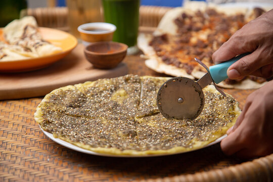 Close up of a hand cutting Zaatar Manakish - Flatbread topped with zaatar and olive oil. Traditional Arab food.