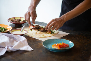 Men's hands preparing and wrapping traditional shawarma wrap or gyro with meat, vegetables and sauces