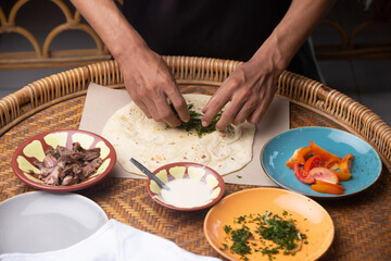 Men's hands preparing and wrapping traditional shawarma wrap or gyro with meat, vegetables and sauces