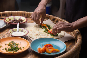 Men's hands preparing and wrapping traditional shawarma wrap or gyro with meat, vegetables and sauces