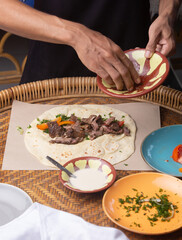 Men's hands preparing and wrapping traditional shawarma wrap or gyro with meat, vegetables and sauces