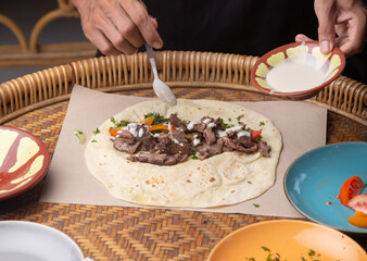 Men's hands preparing and wrapping traditional shawarma wrap or gyro with meat, vegetables and sauces