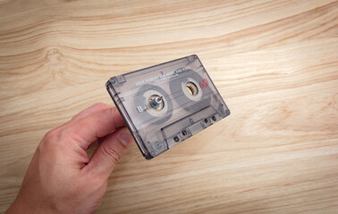 A white man's hand is rewinding cassette tapes on a wooden background..
