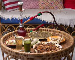 Middle eastern or arabic dishes, assorted meze and hookah on table: pita, Manakish Lahm Bi Ajeen - Flatbreads topped with minced meat, Fatayer stuffed pie and Manakish Zaatar.