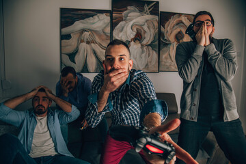 Four happy men playing games and drinking beer while sitting on the sofa.