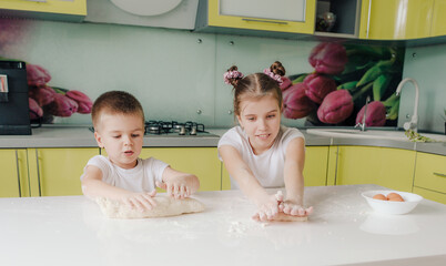 beautiful young brother and sister messing around with dough in the kitchen while cooking. young...