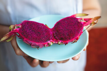 Woman holding a plate with a cut red dragon fruit. It's rich in antioxidants like flavonoids,...