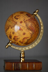 Close-up of a decorative element of the interior of the room - a miniature vintage globe with an old map on a retro book. Gray background