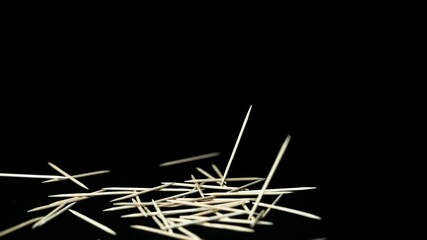 light wooden toothpicks fall in front of black background on dark background slow motion - Powered by Adobe
