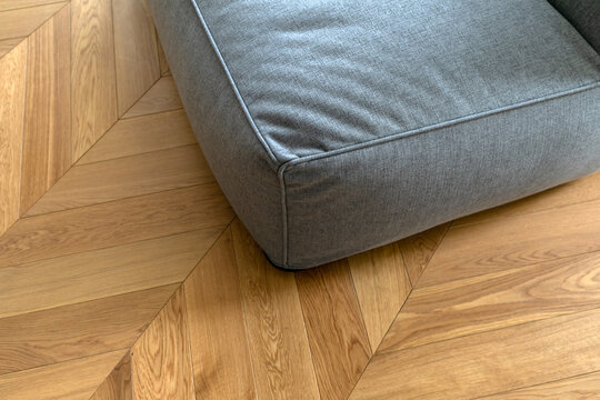 Top view of an textile sofa and french herringbone parquet floor under natural light. Wooden pattern with oak diagonal texture.