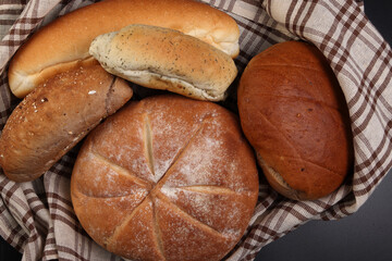 Freshly baked bread loaf bun roll round long mix verity wrapped in checkered kitchen fabric napkin towel over black background