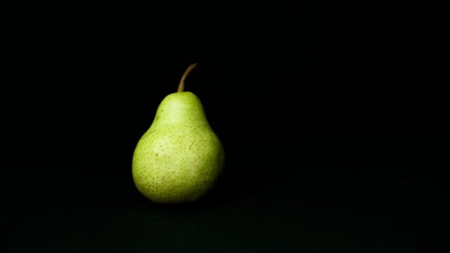 green yellow pear falls clumsily in front of black background on dark background and remains standing slow motion