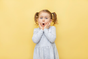 Wow. Closeup portrait of excited child touching her cheeks, over pastel yellow isolated...