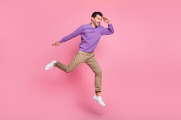 Fototapeta na wymiar Photo of cute sweet young guy wear violet sweater jumping high looking far away empty space isolated pink color background
