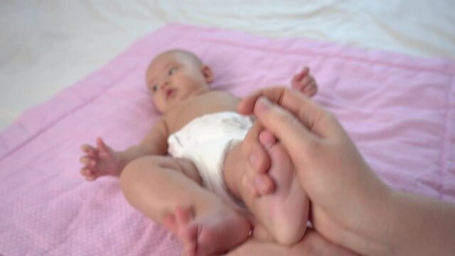 Mom makes a heel massage to a newborn baby lying on the bed