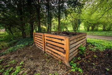 Two-part compost made of wooden slats filled with organic material situated in the shady part of the garden
