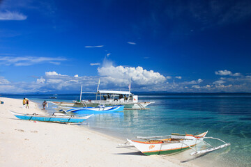 Fototapeta na wymiar wooden boats on the sandy beach at crystal clear blue waters with blue sky in the back at the tropical island Malapascua in the Philippines