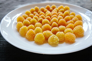 Ripe yellow raspberry lies on a white plate on a black background.