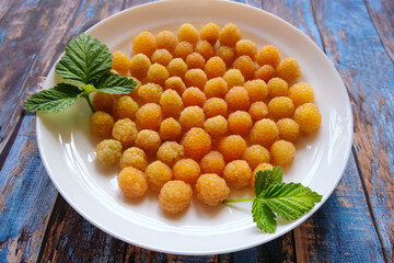 Ripe yellow raspberry lies on a white plate on a blue wooden background.