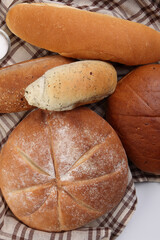 Freshly baked bread loaf bun roll round long mix verity wrapped in checkered kitchen fabric napkin towel over white background