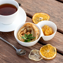 Tasty breakfast. Simple crepe, tea and citrus jam. Delicate thin pancake rolled on plate and saucer with orange jam. Wooden table on background. Top view. Good morning concept.