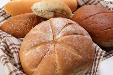 Freshly baked bread loaf bun roll round long mix verity wrapped in checkered kitchen fabric napkin towel over white background