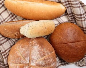 Freshly baked bread loaf bun roll round long mix verity wrapped in checkered kitchen fabric napkin towel over white background