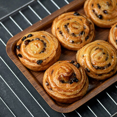 Puff pastry curls cinnamon raisin buns just baked. Fresh baked dough on tray just out of oven. Sweet pastries and desserts concept. Square format. Soft focus.