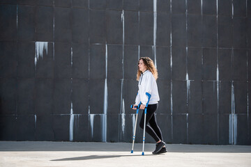 Fototapeta na wymiar Girl with crutches and mask walking alone