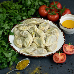 Plate of freshly boiled dumplings with meat filling, tomatoes and melted butter on black wooden table with spoon of spices on it. Cooking process. 