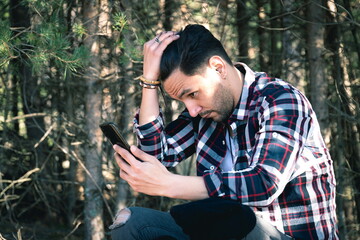 Lumberjack man sitting on a log with mobile phone in command while combing his hair
