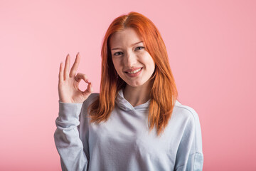 Redhead girl showing Okay gesture in studio on pink background