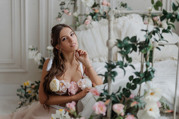 Portrait of a beautiful girl in a pink wedding dress near the bed with spring flowers