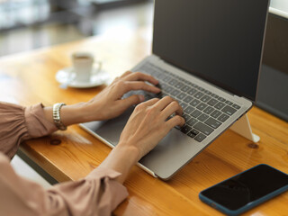 Female worker hands typing on laptop keyboard on wooden desk in cafe