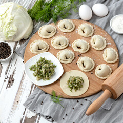 Cabbage and dill green, vegetable filling on rolling Raw dough. Dumplings or ravioli, Cooking process. Top view of Ingredients and rolling pin. Preparation of Convenience Food. Square format 1x1.