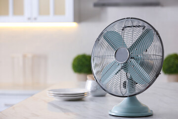 Modern electric fan on countertop in kitchen, space for text. Summer heat - obrazy, fototapety, plakaty