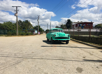 A classic car from the fifties without a license plate or brand, half repaired. Cuban vintage car with worn paint in a rural town.