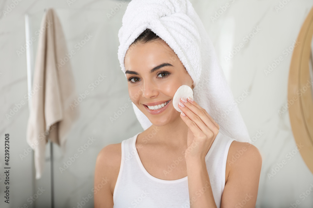 Poster happy young woman cleaning face with cotton pad in bathroom