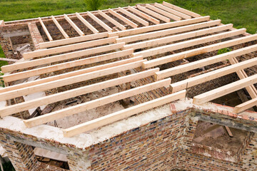 Close up of a brick house with wooden ceiling frame under construction.