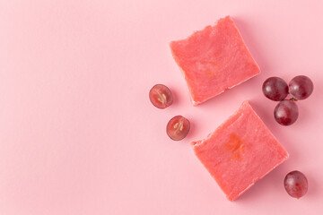 Handmade soap and halves cut red grapes on pink background. Natural fruit toiletry for bath and spa...