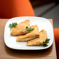 Simple pancakes or crepes with wrapped filling and garnished with herbs on white plate. Traditional breakfast or lunch on wooden table in restaurant. Square format.